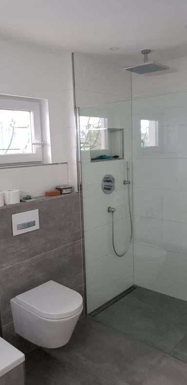 Modernes Bad mit Dusche, WC und großen Fenstern für viel Tageslicht.