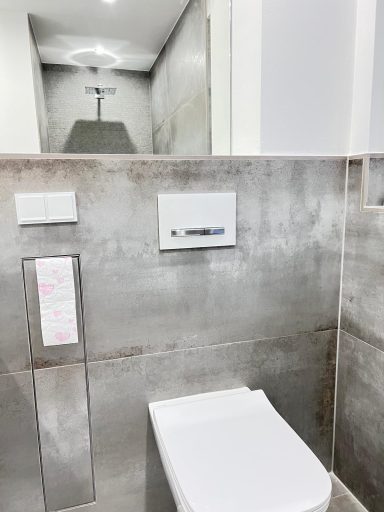 Moderner Badezimmerbereich mit WC, grauen Wänden und minimalistischer Armatur.