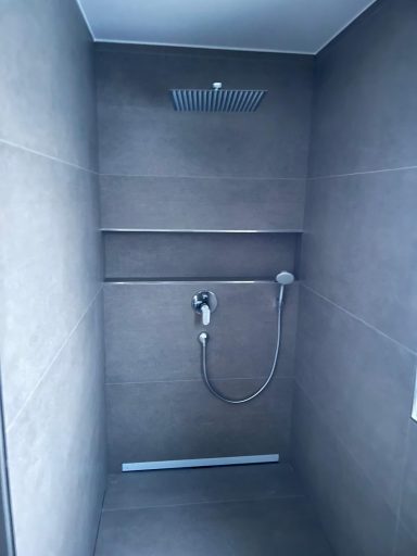 Dusche in einem modernen Badezimmer mit grauen Fliesen und Handbrause.