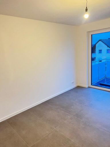 Helle, leere Wohnraum mit Fliesenboden und Fenster zur Terrasse.