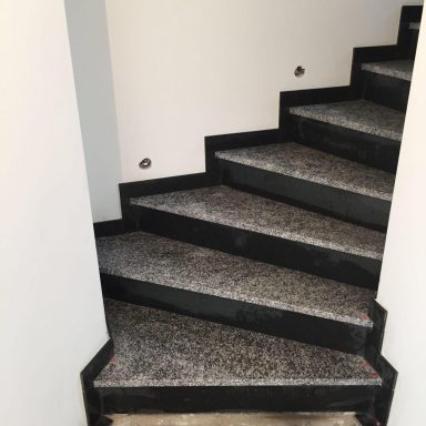 Schwarze Treppenstufen mit grauem Marmorbelag und weißen Wänden.