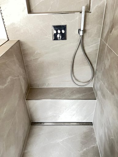 Moderne Dusche mit fliesenverkleideten Wänden und Handbrause.